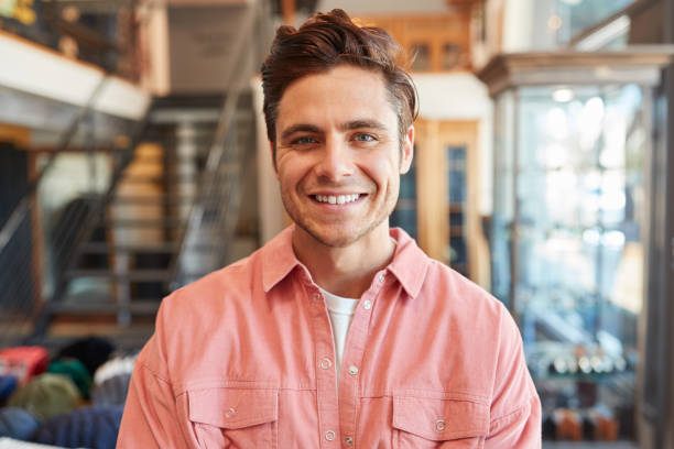 Portrait Of Smiling Male Owner Of Fashion Store Standing In Front Of Clothing Display